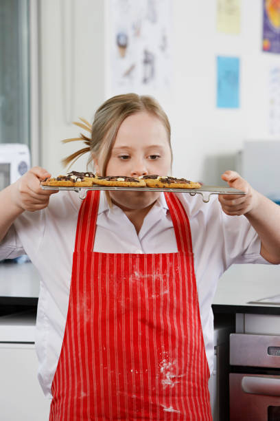 14260064 Girl (10-12) with Down syndrome carrying cookies on baking sheet in kitchen 12 13 years pre adolescent child female blond hair stock pictures, royalty-free photos & images