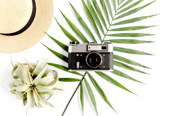 istock Flat lay traveler accessories on white background with retro camera, straw hat, sunglasses, and tropical palm leaf. Travel concept background 1273324941