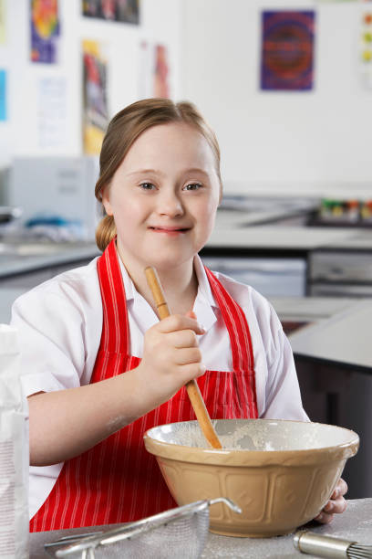 14260059 Portrait of girl (10-12) with Down syndrome mixing contents in bowl 12 13 years pre adolescent child female blond hair stock pictures, royalty-free photos & images