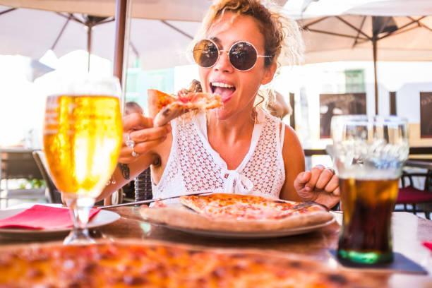 Happy young adult caucasian woman eating a beautiful and tasty healthy pizza at the restaurant - concept of happy people and food relationship - italian style life and summer leisure vacation activity Happy young adult caucasian woman eating a beautiful and tasty healthy pizza at the restaurant - concept of happy people and food relationship - italian style life and summer leisure vacation activity puerto de la cruz tenerife stock pictures, royalty-free photos & images