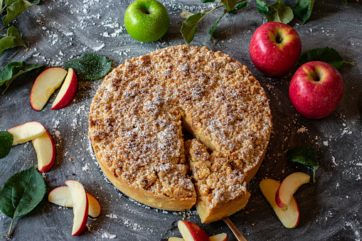 fresh and homemade apple crumble cake - baked in a springform pan and served on a dark table - ready to eat
