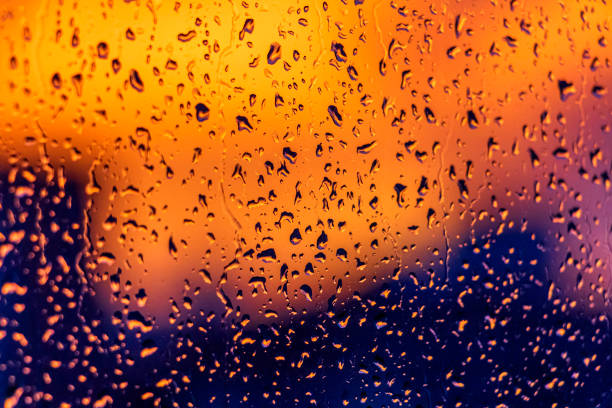 istock Bright fiery sunset through raindrops on window with bokeh lights. Abstract background. Water drop on the glass against the blurred silhouettes high-rise city. 1273329039