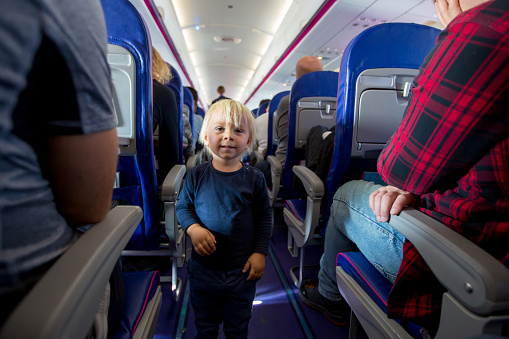 Cute toddler boy in airtplane, playing on the path between the seats, smiling happily. Family travel with kids concept
