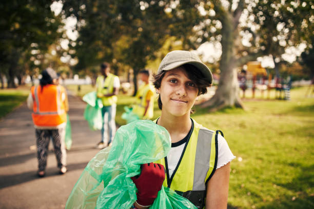 I love my volunteer work Cropped portrait of a young female volunteer doing community service in the local park with her friends in the background social responsibility photos stock pictures, royalty-free photos & images