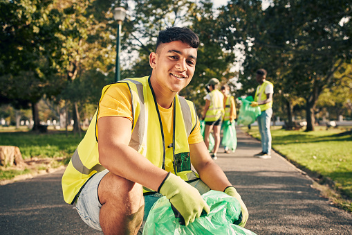 Cropped portrait of a young male volunteer doing community service in the local park with his friends in the background