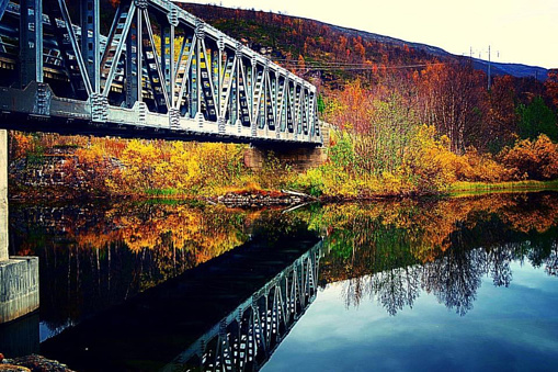 Metal bridge with perfect reflection in river surrounded by intense autumn colours in nature. The photo is captured outside Bardu in Troms county in North of Norway.