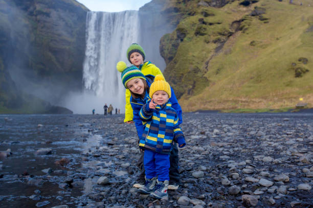 cute children playing in front of the skogafoss waterfall in iceland on a sunset cloudy day - gullfoss falls imagens e fotografias de stock