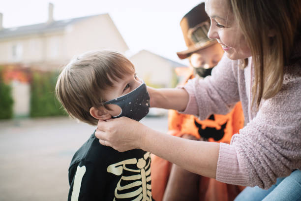 мать положить защитную маску на своего ребенка во время пандемии covid-19 на хэллоуин - child autumn scarecrow decoration стоковые фото и изображения