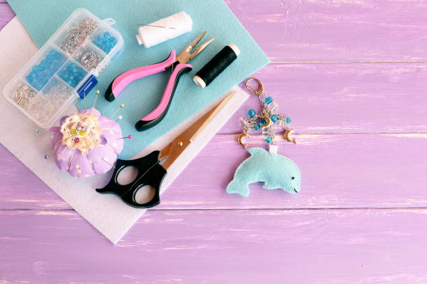 istock Cute felt dolphin with beads. Handmade felt keychain for bag charm. Beads, thread, needle, scissors, pliers, pincushion, pins. Wooden background. Crafts supplies and tools 1273336171
