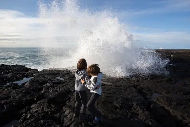 Photo of Children watching big waves crashing in rocks on the south west coast on Iceland