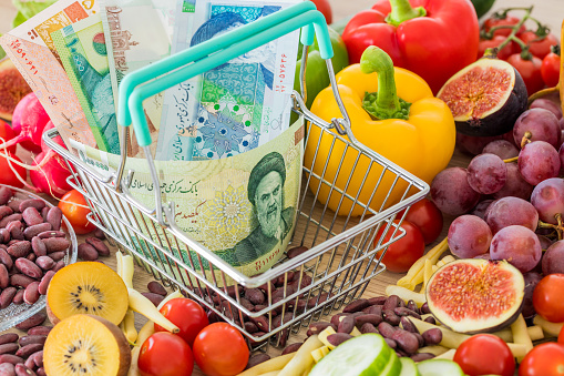Shopping basket with Iranian money, around food products, vegetables and fruits. The concept of inflation, rising prices and more expensive food