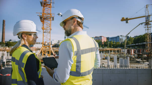 istock Male Civil Engineer and Young Female Building Architect Use a Tablet Computer on a City Construction Site. They Talk About the Future of Real Estate Development and Planning. Wearing Safety Hard Hats. 1273337023