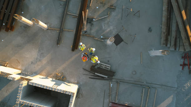 istock Aerial Top Down Shot of a Constructions Site with Diverse Team of Engineers and Worker with Theodolite Looking Up and Smiling. Heavy Machinery and Construction Workers are Working in the Area. 1273337070
