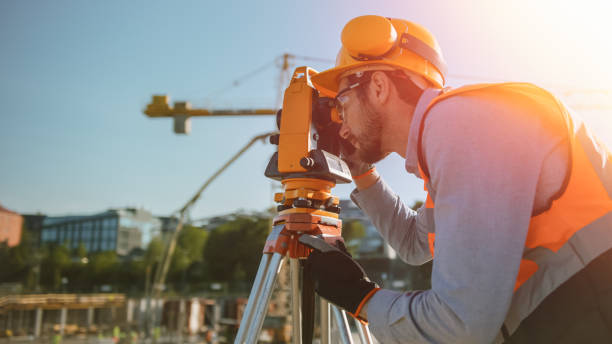 istock Construction Worker Using Theodolite Surveying Optical Instrument for Measuring Angles in Horizontal and Vertical Planes on Construction Site. Worker in Hard Hat Making Projections for the Building. 1273337108