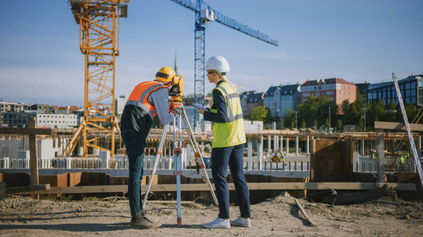 istock Construction Worker Using Theodolite Surveying Optical Instrument for Measuring Angles in Horizontal and Vertical Planes on Construction Site. Engineer and Architect Using Tablet Next to Surveyor. 1273337288