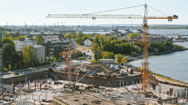 istock Aerial Shot of a New Constructions Development Site with High Tower Cranes Building Real Estate. Heavy Machinery and Construction Workers are Employed. Blue Sea and City Houses in the Background. 1273337662