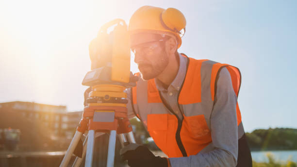 istock Construction Worker Using Theodolite Surveying Optical Instrument for Measuring Angles in Horizontal and Vertical Planes on Construction Site. Worker in Hard Hat Making Projections for the Building. 1273337666