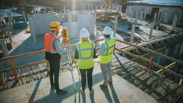 istock Construction Worker Using Theodolite Surveying Optical Instrument for Measuring Angles in Horizontal and Vertical Planes on Construction Site. Engineer and Architect Using Tablet Next to Surveyor. 1273337711
