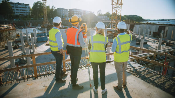 istock Construction Worker Using Theodolite Surveying Optical Instrument for Measuring Angles in Horizontal and Vertical Planes on Construction Site. Engineers and Architect Discuss Plans Next to Surveyor. 1273337758