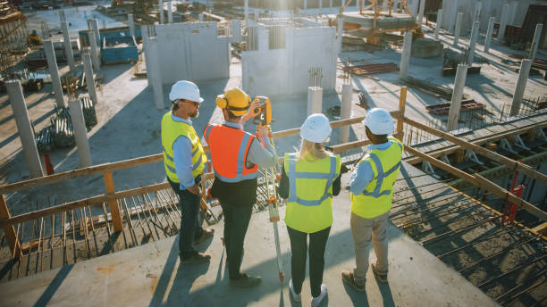 istock Construction Worker Using Theodolite Surveying Optical Instrument for Measuring Angles in Horizontal and Vertical Planes on Construction Site. Engineers and Architect Discuss Plans Next to Surveyor. 1273337759