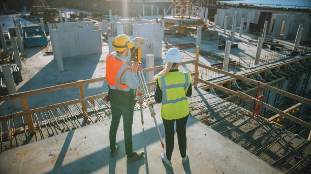istock Construction Worker Using Theodolite Surveying Optical Instrument for Measuring Angles in Horizontal and Vertical Planes on Construction Site. Engineer and Architect Using Tablet Next to Surveyor. 1273337808