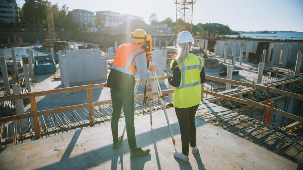 istock Construction Worker Using Theodolite Surveying Optical Instrument for Measuring Angles in Horizontal and Vertical Planes on Construction Site. Engineer and Architect Using Tablet Next to Surveyor. 1273337838
