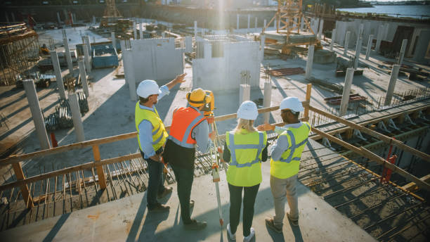 istock Construction Worker Using Theodolite Surveying Optical Instrument for Measuring Angles in Horizontal and Vertical Planes on Construction Site. Engineers and Architect Discuss Plans Next to Surveyor. 1273337844