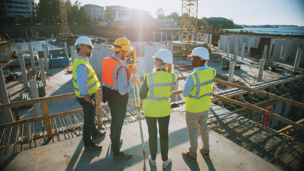 istock Construction Worker Using Theodolite Surveying Optical Instrument for Measuring Angles in Horizontal and Vertical Planes on Construction Site. Engineers and Architect Discuss Plans Next to Surveyor. 1273337884