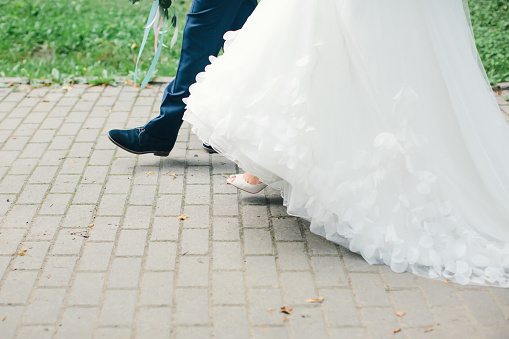 Couple is walking along road in one direction. Legs of bride and groom close-up.