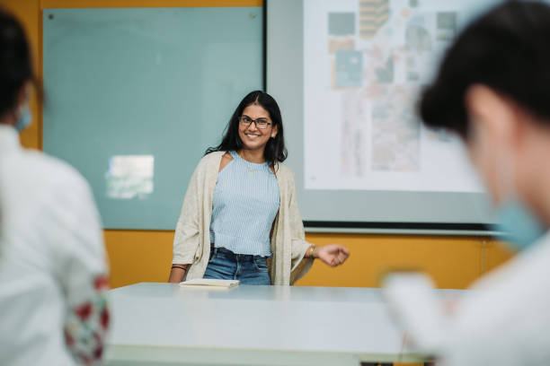 Asian indian smiling female student presenting in college classroom college student is making a presentation in front of projector screen projector screen classroom stock pictures, royalty-free photos & images