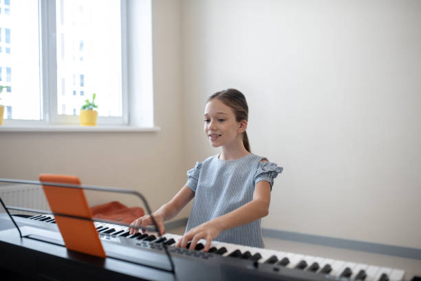 Long-haired girl in blue dress sitting at the synthesizer and playing Playing. Long-haired girl in blue dress sitting at the synthesizer and playing girl playing piano stock pictures, royalty-free photos & images