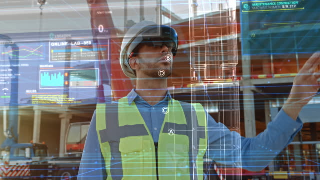 Futuristic Architectural Engineer Wearing Augmented Reality Headset, Uses Gestures to Create 3D Graphics VFX Model of a Building with Infographics. In Background Construction Site in Progress