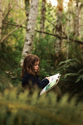 A little girl reads her book outside on a log