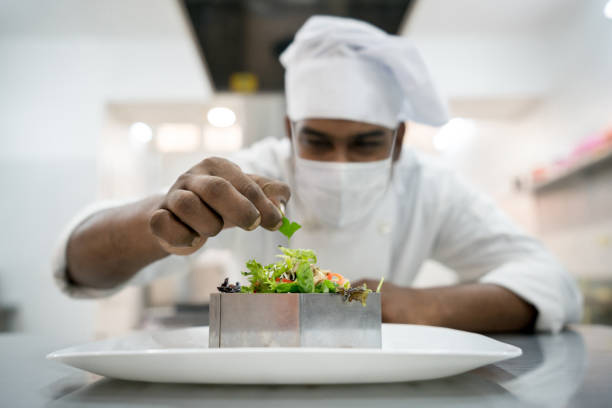 istock Indian chef wearing a facemask at a restaurant while decorating a plate 1273354328