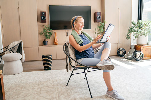 Caucasian senior woman sitting in her sportswear in living room. she is watching online gym exercises