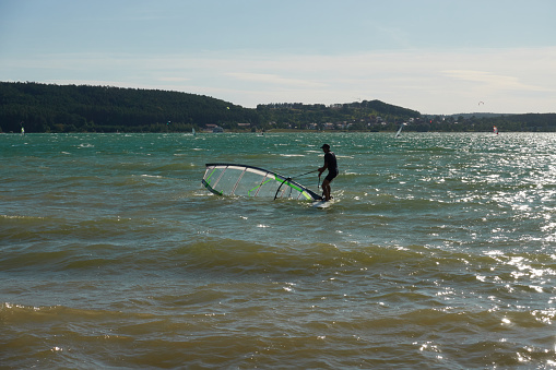 Allmannsdorf, Germany - August 26, 2020: Wind surfer moves the sail of his board out of the water. Brombachsee, Pleinfeld.