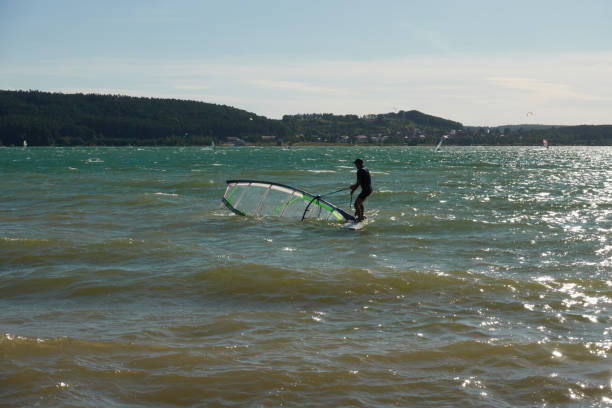 Wind surfer moves the sail of his board out of the water. Brombachsee, Pleinfeld. Allmannsdorf, Germany - August 26, 2020: Wind surfer moves the sail of his board out of the water. Brombachsee, Pleinfeld. kiteboarding stock pictures, royalty-free photos & images