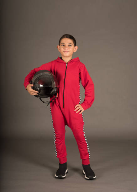 a boy wears red racing costume and he is holding helmet
