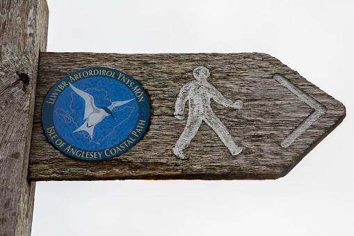 A sign in both the Welsh and English languages, pointing people to the direction of the Isle of Anglesey Coastal Path in North Wales, UK.