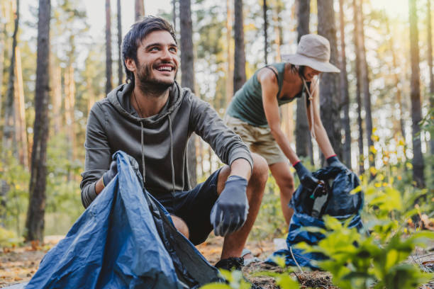 Cheerful mixed race man looking away while collecting trash with friends outdoor Cheerful mixed race man looking away while collecting trash with friends outdoor plastic pollution photos stock pictures, royalty-free photos & images