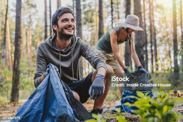 Cheerful Mixed Race Man Looking Away While Collecting Trash With Friends Outdoor Stock Photo - Download Image Now