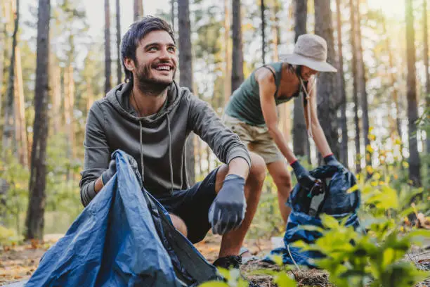 Cheerful mixed race man looking away while collecting trash with friends outdoor