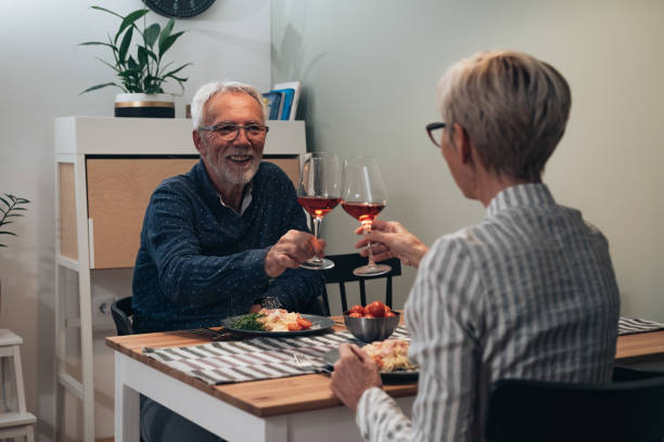 happy senior couple toasting at dining table stock photo - eating senior adult color image spaghetti imagens e fotografias de stock