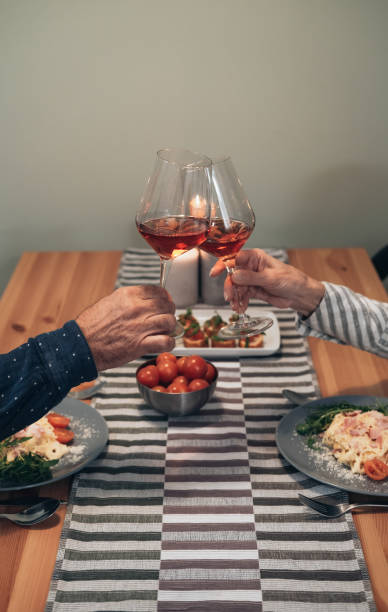 close up of senior couple toasting with wine at dining table stock photo - eating senior adult color image spaghetti imagens e fotografias de stock