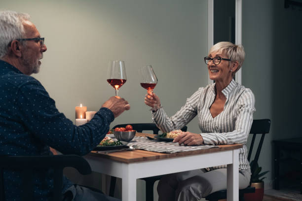 happy senior couple toasting at dining table stock photo - eating senior adult color image spaghetti imagens e fotografias de stock