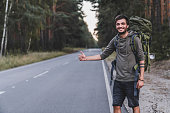 Caucasian young male traveller try to catch car on forest road. World travel road trip, holiday hitch hike concept