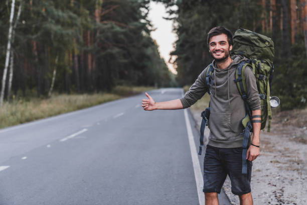 Caucasian young male traveller try to catch car on forest road. World travel road trip, holiday hitch hike concept Caucasian young male traveller try to catch car on forest road. World travel road trip, holiday hitch hike concept hitchhiking stock pictures, royalty-free photos & images