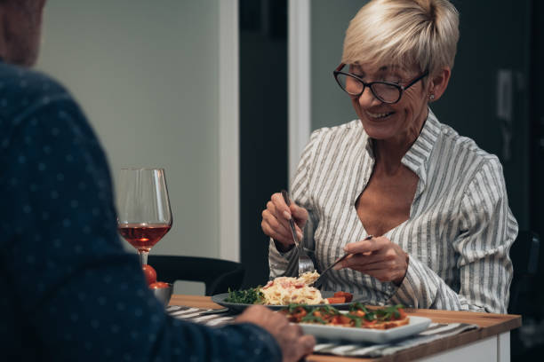 couples joyeux ont le dîner romantique à la photo de stock à la maison - eating senior adult color image spaghetti photos et images de collection