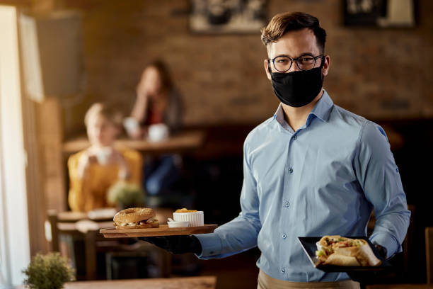istock Happy waiter serving food while wearing protective face mask in a pub. 1273371495