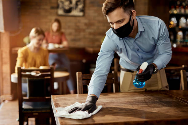 istock Waiter with protective face mask disinfecting tables in a pub. 1273371689
